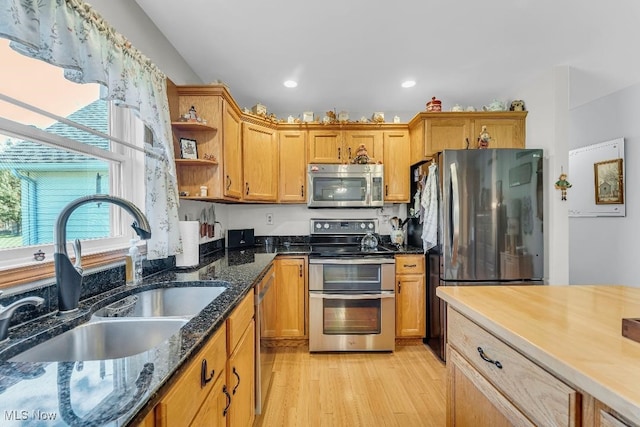 kitchen featuring appliances with stainless steel finishes, light wood-type flooring, dark stone countertops, and sink