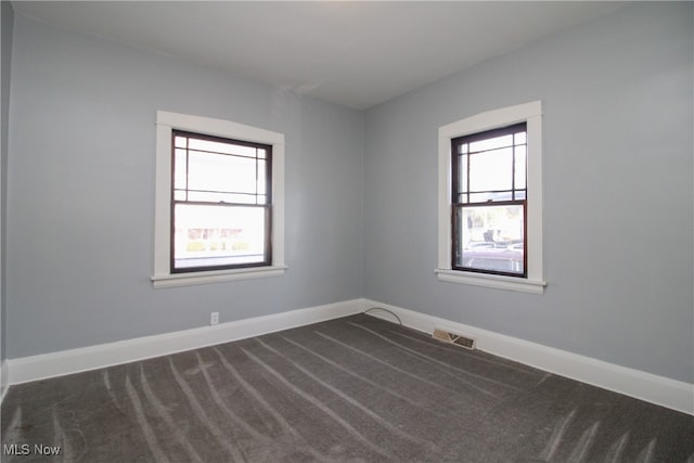 empty room featuring a wealth of natural light and dark carpet