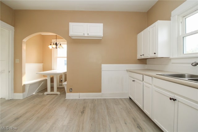 kitchen with sink, decorative light fixtures, white cabinets, light hardwood / wood-style flooring, and a chandelier