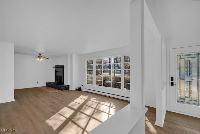 living room featuring a baseboard radiator, ceiling fan, a wood stove, and wood-type flooring