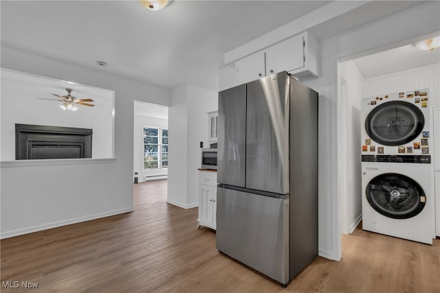 kitchen featuring light hardwood / wood-style floors, appliances with stainless steel finishes, stacked washer and dryer, and white cabinets