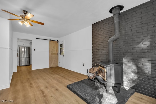 living room featuring light hardwood / wood-style flooring, ceiling fan, a barn door, and a wood stove