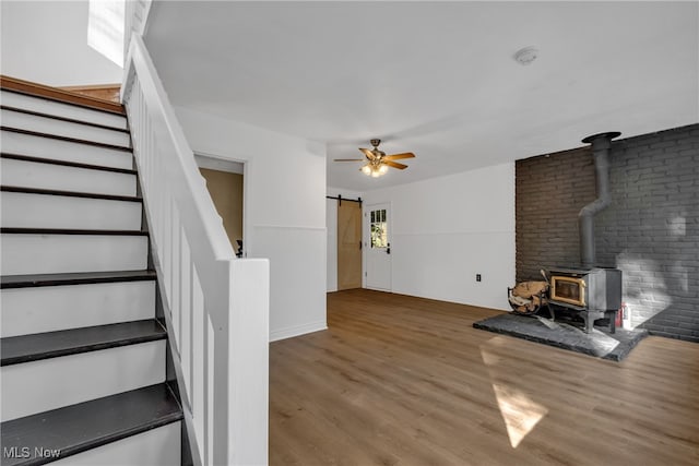 interior space with brick wall, a barn door, wood-type flooring, and a wood stove