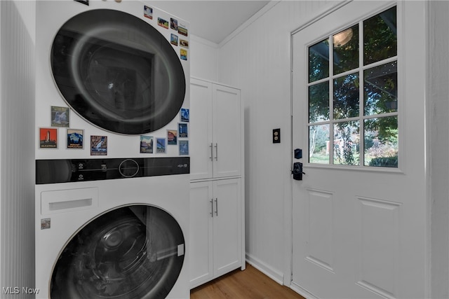 clothes washing area with stacked washer / drying machine, crown molding, cabinets, and light hardwood / wood-style floors