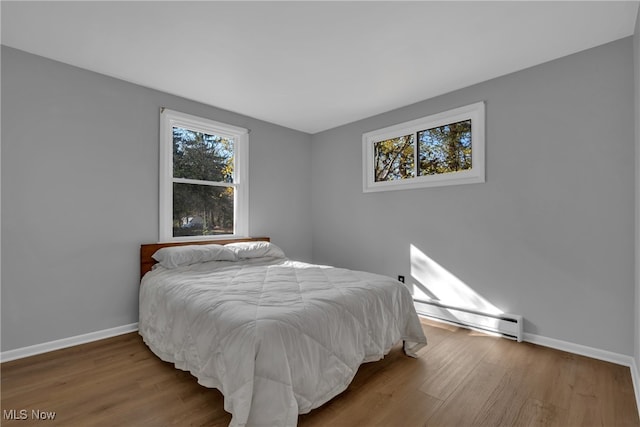 bedroom with wood-type flooring and a baseboard heating unit