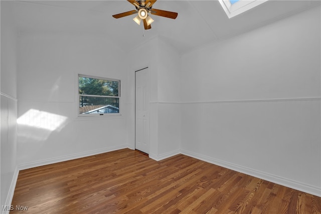 empty room featuring ceiling fan, wood-type flooring, and vaulted ceiling with skylight