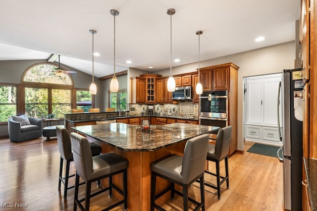 kitchen with dark stone counters, hanging light fixtures, light hardwood / wood-style flooring, vaulted ceiling, and stainless steel appliances