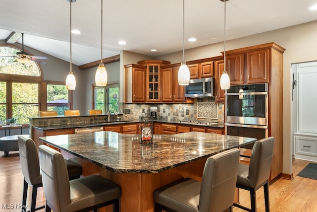 kitchen with lofted ceiling with beams, a kitchen breakfast bar, light hardwood / wood-style flooring, appliances with stainless steel finishes, and decorative light fixtures