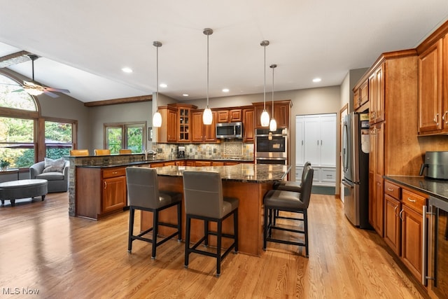 kitchen featuring appliances with stainless steel finishes, light hardwood / wood-style flooring, a breakfast bar area, hanging light fixtures, and lofted ceiling