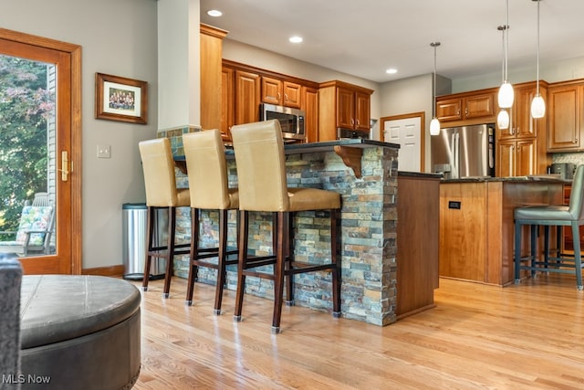 bar with dark stone countertops, pendant lighting, light wood-type flooring, and appliances with stainless steel finishes