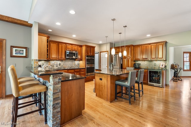 kitchen featuring a center island, a kitchen breakfast bar, appliances with stainless steel finishes, light hardwood / wood-style floors, and beverage cooler