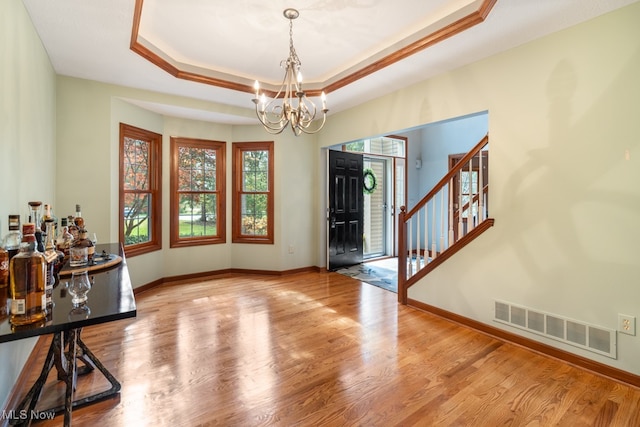 entrance foyer with a raised ceiling, wood-type flooring, and a chandelier