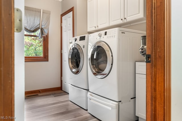 clothes washing area with washer and clothes dryer, cabinets, and light hardwood / wood-style flooring