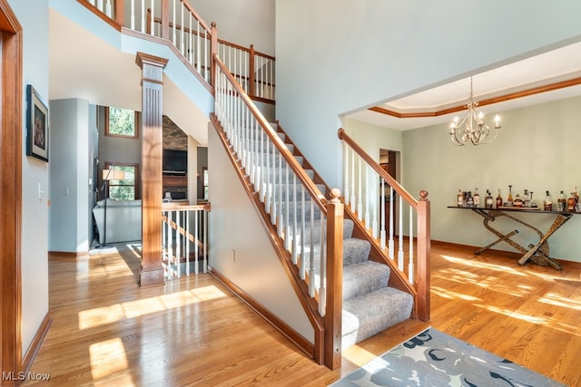 staircase featuring a chandelier, wood-type flooring, a towering ceiling, and a tray ceiling