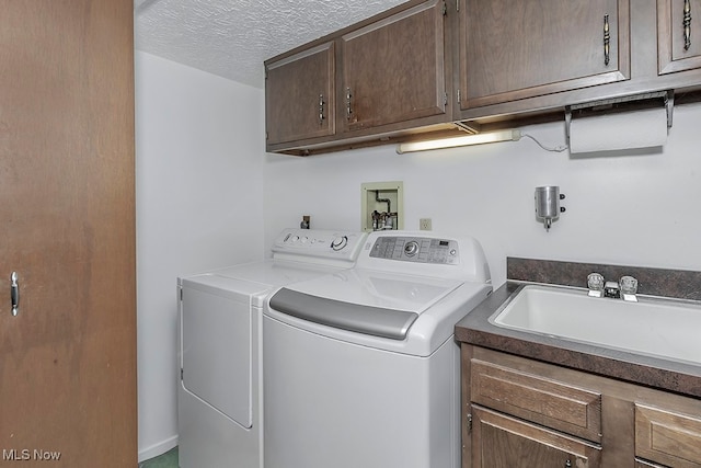 clothes washing area with cabinets, a textured ceiling, sink, and washing machine and dryer