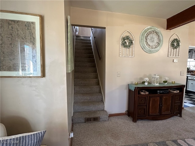 stairs with beamed ceiling and carpet flooring