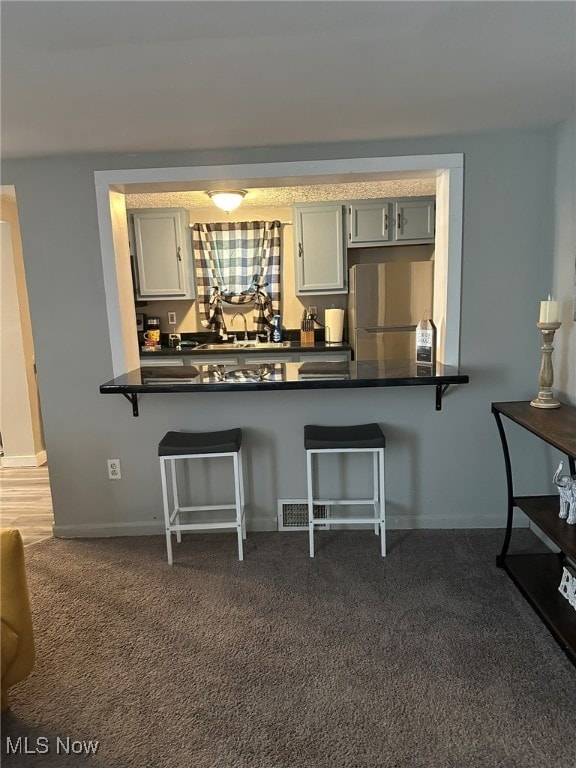 kitchen with gray cabinets, kitchen peninsula, dark colored carpet, and stainless steel fridge