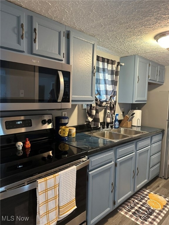 kitchen with appliances with stainless steel finishes, a textured ceiling, hardwood / wood-style flooring, gray cabinetry, and sink