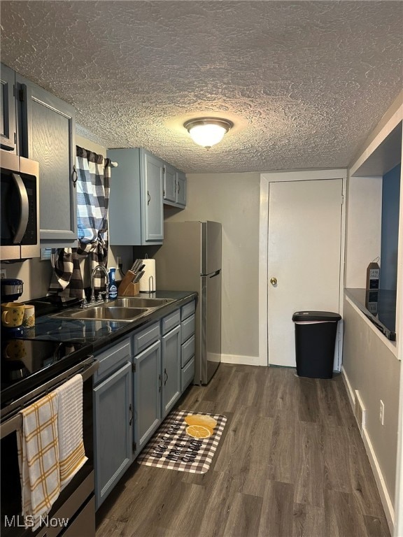 kitchen with appliances with stainless steel finishes, a textured ceiling, dark wood-type flooring, gray cabinets, and sink