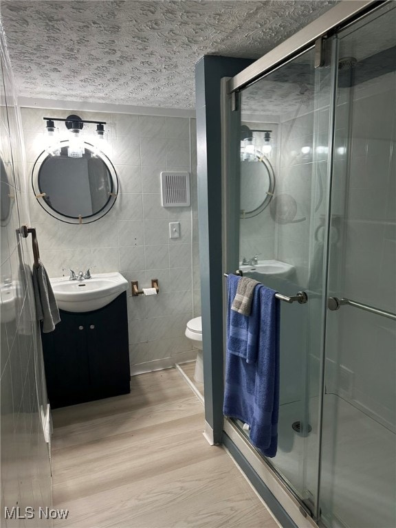 bathroom featuring toilet, a shower with shower door, wood-type flooring, vanity, and tile walls