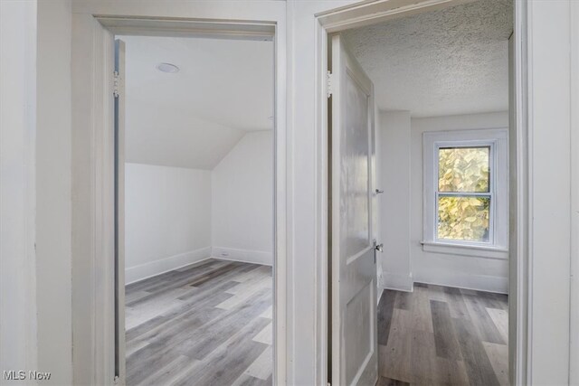 hallway featuring vaulted ceiling, a textured ceiling, and light wood-type flooring