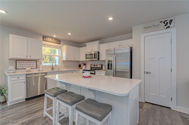 kitchen with a kitchen island, appliances with stainless steel finishes, light hardwood / wood-style flooring, and white cabinets