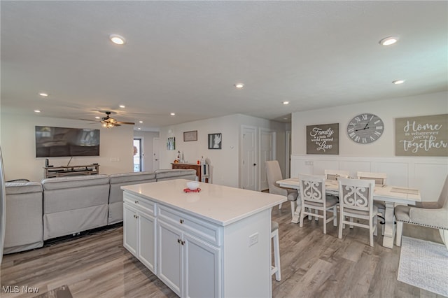 kitchen featuring light wood-type flooring, a kitchen island, ceiling fan, white cabinets, and a breakfast bar area