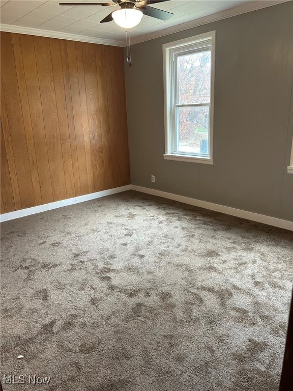 empty room featuring ornamental molding, wooden walls, carpet floors, and ceiling fan