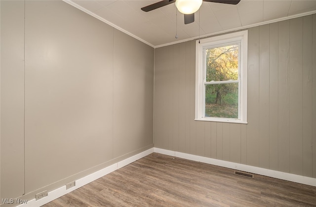 spare room featuring ornamental molding, wood walls, hardwood / wood-style flooring, and ceiling fan