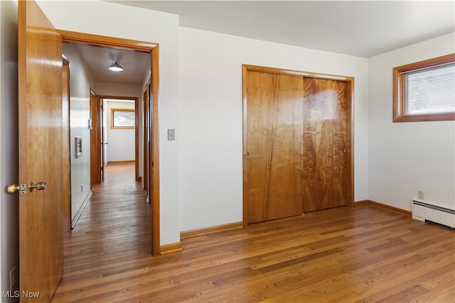 unfurnished bedroom featuring a closet, a baseboard radiator, and hardwood / wood-style floors