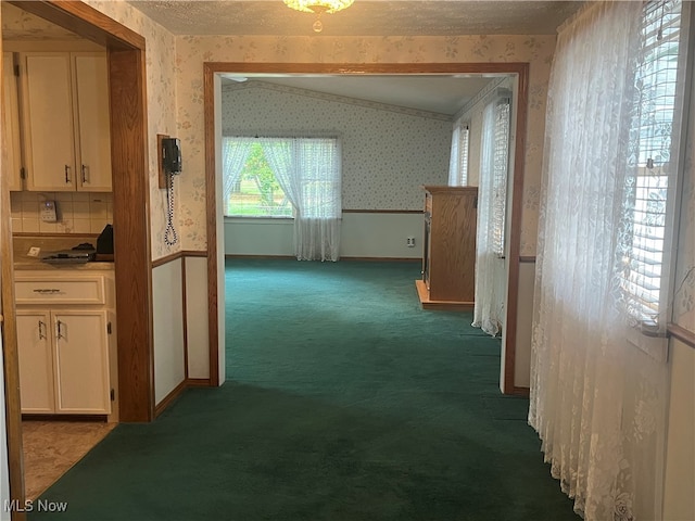 corridor featuring dark carpet, vaulted ceiling, and a textured ceiling