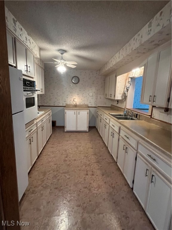 kitchen with white cabinets, ceiling fan, a textured ceiling, sink, and white appliances