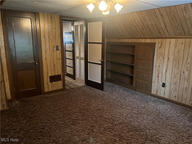 interior space featuring lofted ceiling, wooden walls, and dark colored carpet