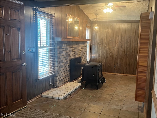 interior space featuring lofted ceiling, ceiling fan, a textured ceiling, a wood stove, and wooden walls