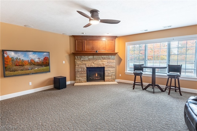 living room with a stone fireplace, carpet flooring, and ceiling fan