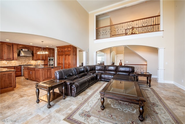 living room featuring a chandelier, decorative columns, ornamental molding, a high ceiling, and sink