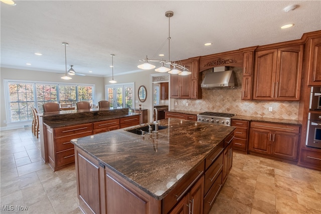 kitchen featuring sink, wall chimney exhaust hood, pendant lighting, crown molding, and a center island with sink