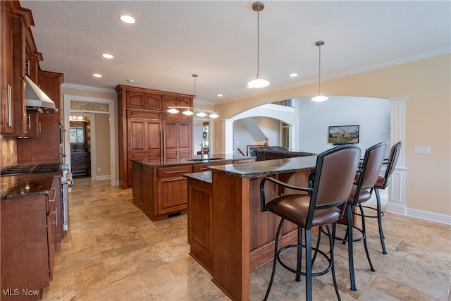 kitchen featuring a kitchen island, dark stone counters, ornamental molding, pendant lighting, and range hood