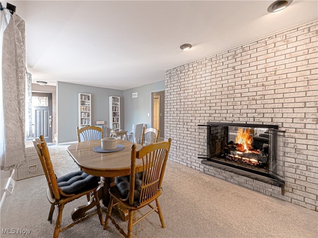 dining area with light carpet, a brick fireplace, and brick wall