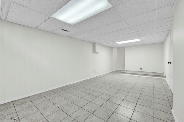 basement with a paneled ceiling, wooden walls, and light tile patterned floors