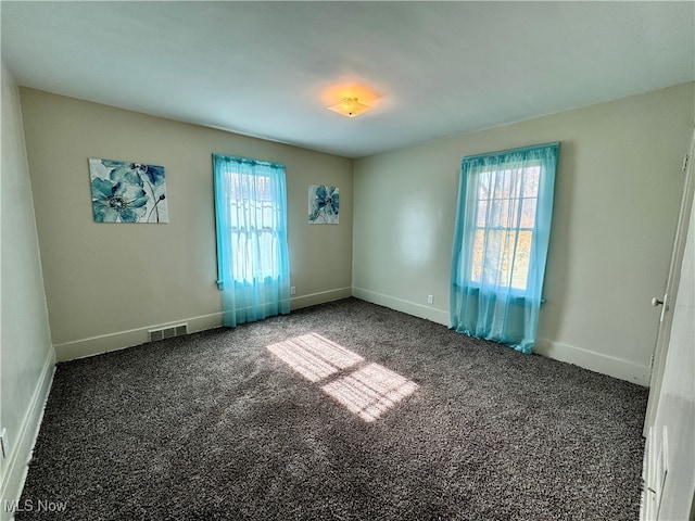 spare room with dark colored carpet and a healthy amount of sunlight