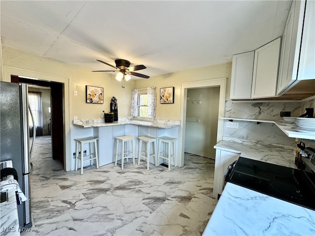 kitchen featuring decorative backsplash, a kitchen breakfast bar, white cabinetry, stainless steel refrigerator, and electric range oven