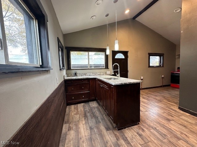 kitchen with light stone counters, decorative light fixtures, hardwood / wood-style floors, sink, and kitchen peninsula