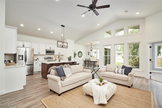 living room featuring light hardwood / wood-style floors, ceiling fan with notable chandelier, sink, and high vaulted ceiling