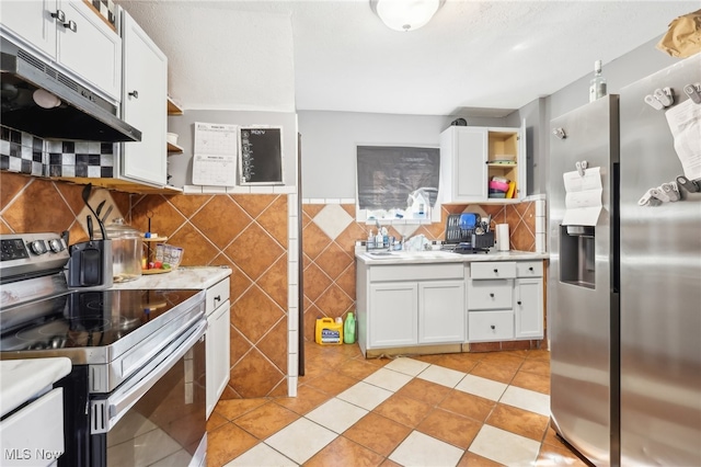 kitchen featuring appliances with stainless steel finishes, white cabinetry, tile walls, and light tile patterned floors