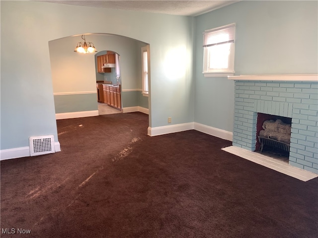 unfurnished living room featuring dark carpet, a brick fireplace, and a textured ceiling