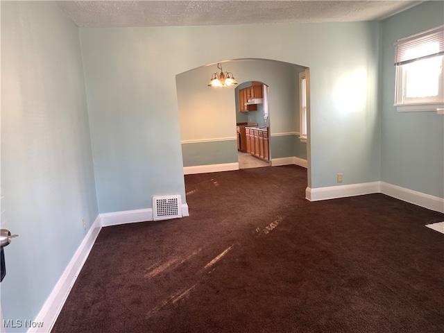 carpeted spare room featuring a textured ceiling and an inviting chandelier