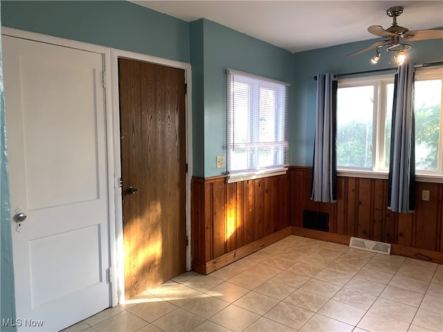 interior space featuring ceiling fan, light tile patterned floors, and wood walls