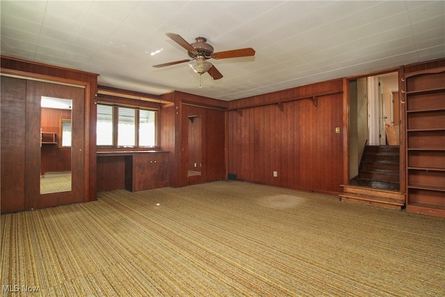 unfurnished living room featuring ceiling fan, wood walls, and light carpet