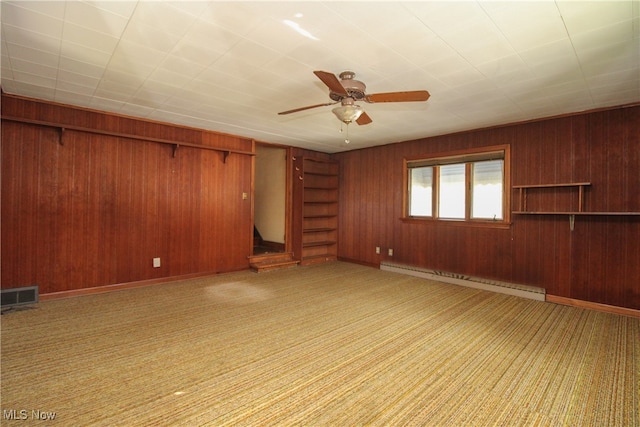 unfurnished living room with ceiling fan, a baseboard heating unit, wooden walls, and light colored carpet